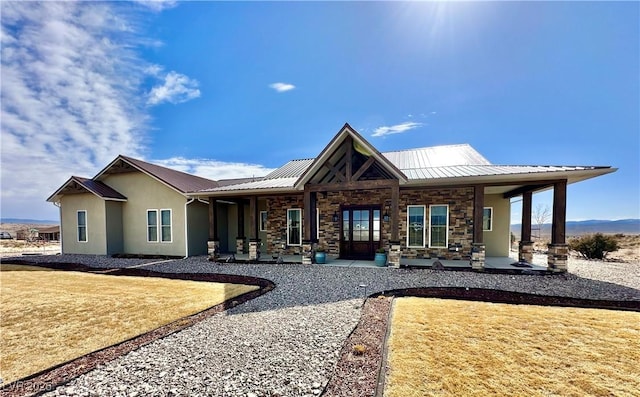 back of house with stucco siding, a porch, a lawn, metal roof, and stone siding