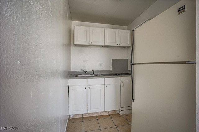 kitchen featuring light tile patterned flooring, a sink, freestanding refrigerator, and white cabinetry