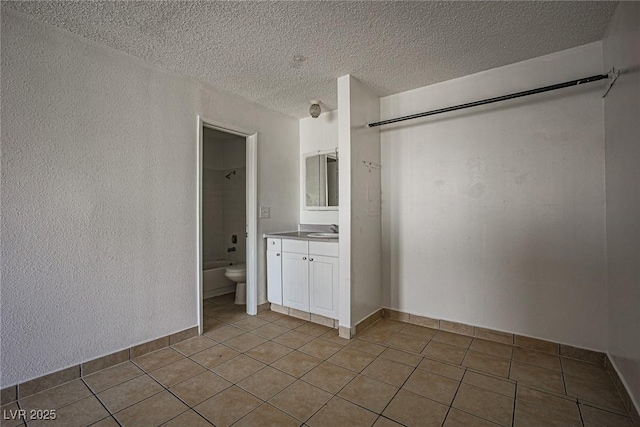 unfurnished bedroom featuring ensuite bathroom, a textured wall, a textured ceiling, light tile patterned flooring, and a sink