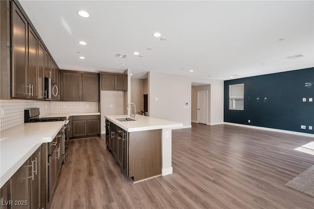 kitchen with wood finished floors, a sink, dark brown cabinets, appliances with stainless steel finishes, and decorative backsplash