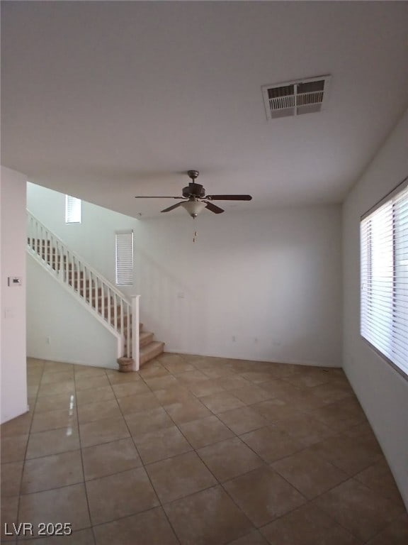 empty room featuring stairs, ceiling fan, tile patterned flooring, and visible vents