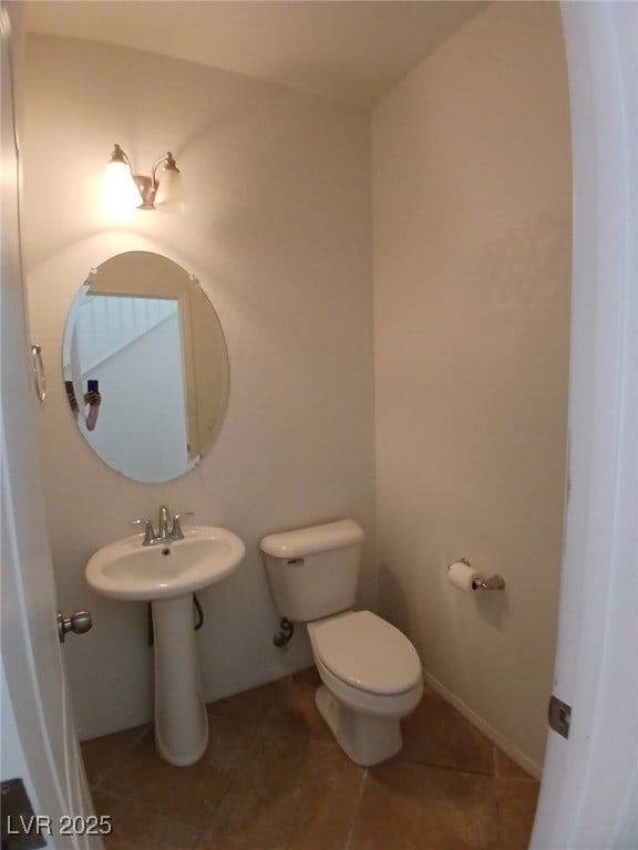 half bath featuring baseboards, toilet, and tile patterned floors