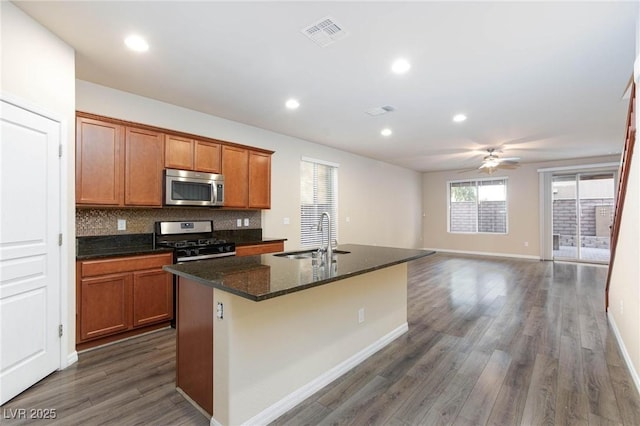 kitchen with stainless steel appliances, a sink, visible vents, decorative backsplash, and an island with sink