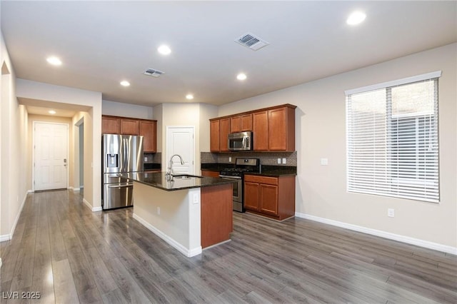 kitchen with dark wood finished floors, stainless steel appliances, dark countertops, tasteful backsplash, and a sink