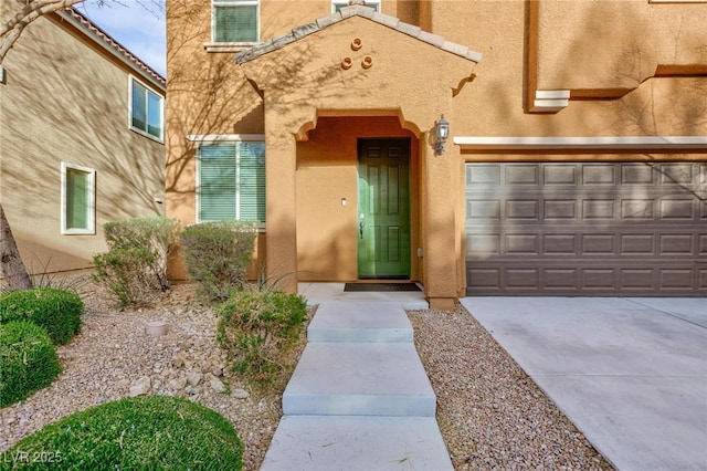 view of exterior entry with a garage, concrete driveway, and stucco siding