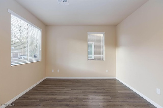 unfurnished room with baseboards, visible vents, and dark wood-style flooring