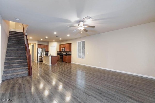 unfurnished living room with visible vents, dark wood finished floors, a sink, and stairs