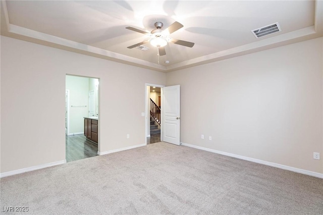 spare room with stairs, visible vents, a tray ceiling, and carpet flooring