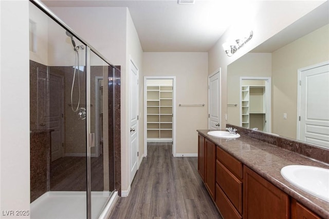 full bath featuring a stall shower, double vanity, a sink, and wood finished floors