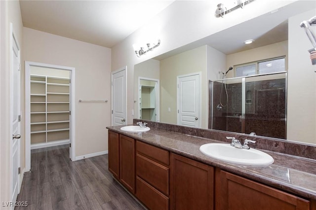 full bathroom featuring a spacious closet, double vanity, a stall shower, and a sink