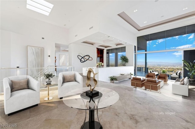 living area with visible vents, a wall of windows, a skylight, and a towering ceiling