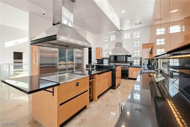 kitchen with light brown cabinets, a sink, wall chimney range hood, and island range hood