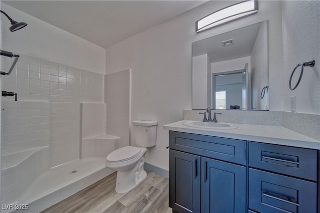 bathroom featuring visible vents, tiled shower, toilet, wood finished floors, and vanity