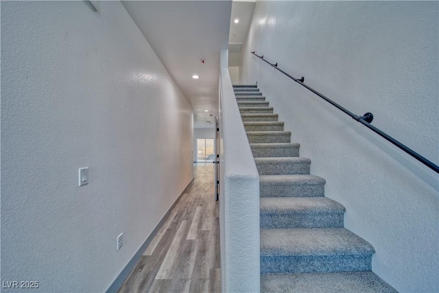 stairway featuring a textured wall, wood finished floors, and recessed lighting