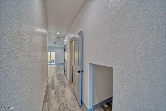 hallway with a textured wall, light wood finished floors, and recessed lighting