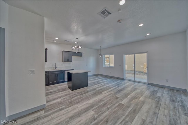kitchen with a sink, baseboards, light countertops, a center island, and light wood finished floors