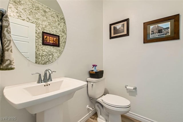 bathroom with toilet, wood finished floors, baseboards, and a sink