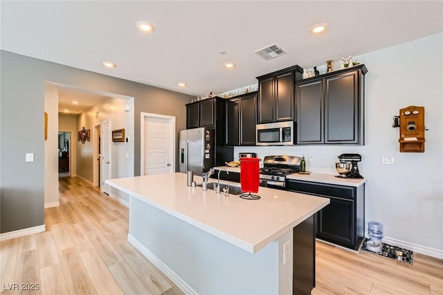 kitchen featuring visible vents, a center island with sink, a sink, light wood-style floors, and appliances with stainless steel finishes