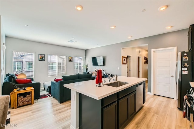 kitchen featuring light wood finished floors, open floor plan, light countertops, appliances with stainless steel finishes, and a sink