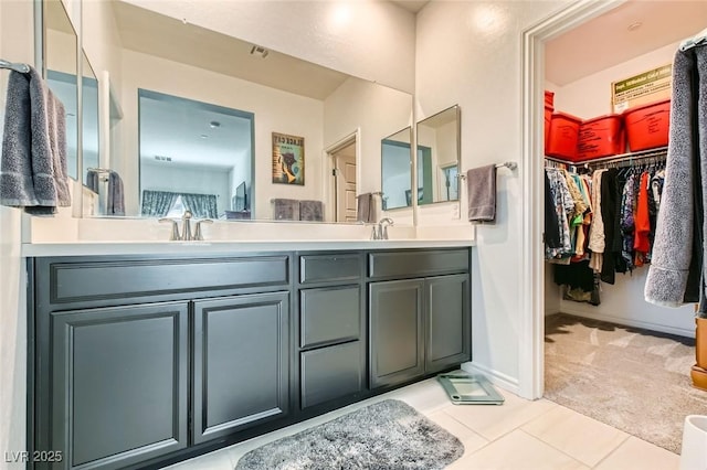 full bathroom with tile patterned flooring, a walk in closet, baseboards, double vanity, and a sink