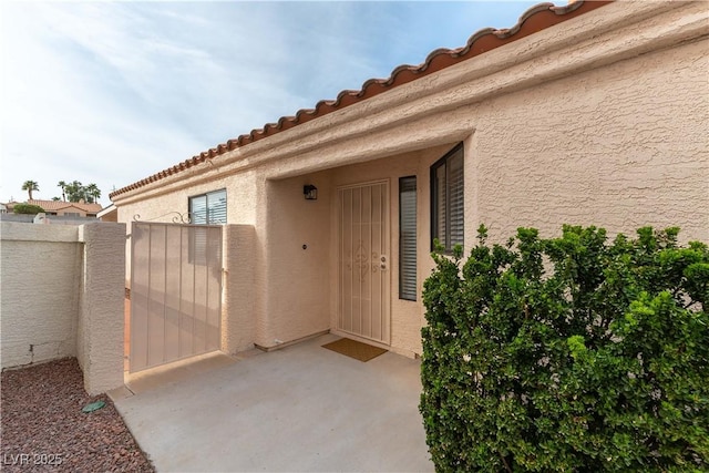 view of exterior entry featuring a patio area, a gate, fence, and stucco siding