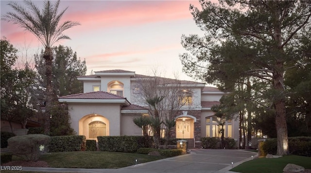 mediterranean / spanish-style house featuring concrete driveway, a yard, a tile roof, and stucco siding