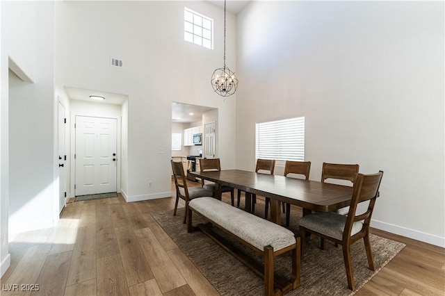 dining area with a chandelier, baseboards, visible vents, and light wood finished floors