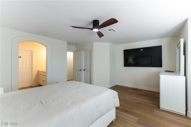 bedroom featuring arched walkways, light wood-style flooring, a ceiling fan, visible vents, and baseboards