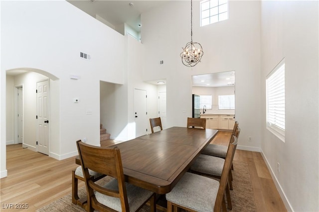 dining area with light wood-type flooring, visible vents, arched walkways, and baseboards