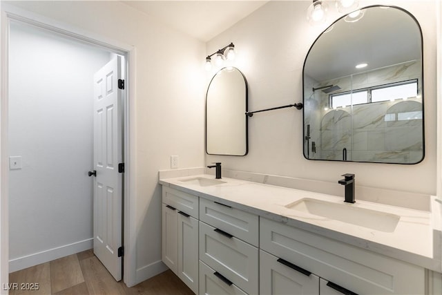 full bathroom with a marble finish shower, baseboards, a sink, and wood finished floors