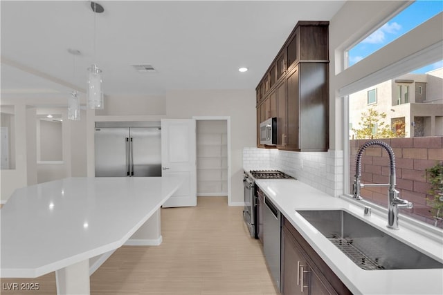 kitchen with a sink, visible vents, dark brown cabinets, appliances with stainless steel finishes, and light countertops