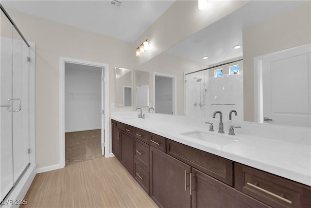 bathroom featuring double vanity, a sink, a walk in closet, and a shower stall