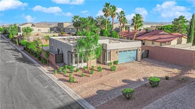 view of front facade with decorative driveway, stucco siding, fence, a garage, and a residential view