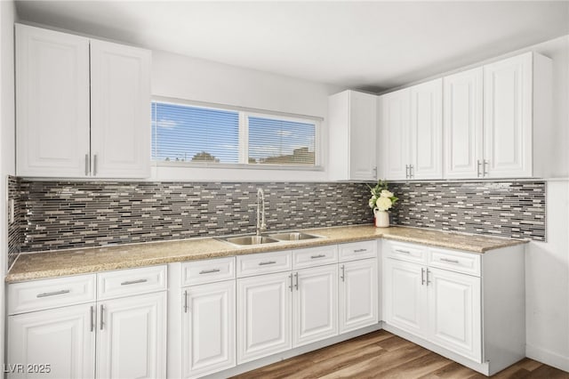 kitchen featuring light countertops, backsplash, light wood-style flooring, white cabinets, and a sink