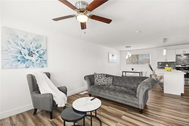 living room featuring ceiling fan with notable chandelier, wood finished floors, and baseboards