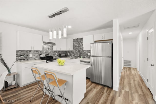 kitchen featuring under cabinet range hood, white cabinets, appliances with stainless steel finishes, light wood-type flooring, and a center island