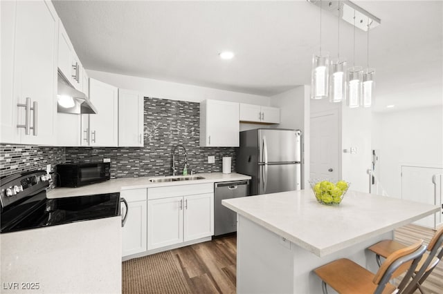 kitchen with stainless steel appliances, light countertops, white cabinetry, a sink, and a kitchen bar