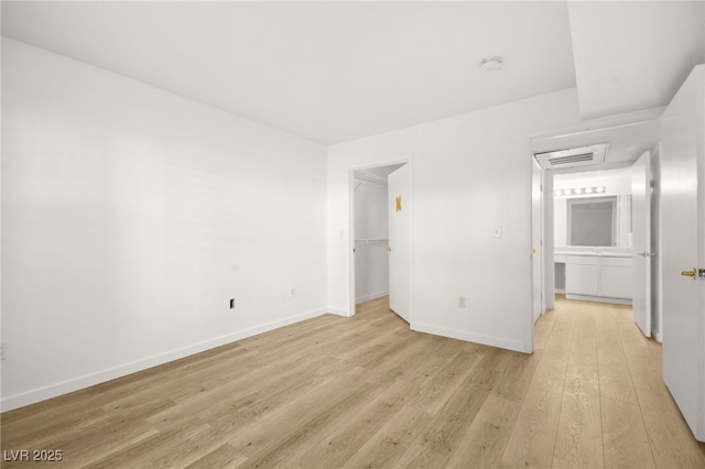 unfurnished bedroom with baseboards, a closet, a walk in closet, and light wood-style floors