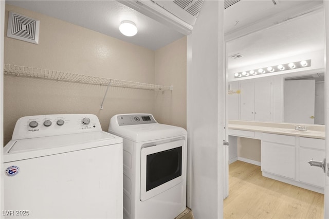 clothes washing area featuring laundry area, light wood finished floors, visible vents, washer and dryer, and a sink