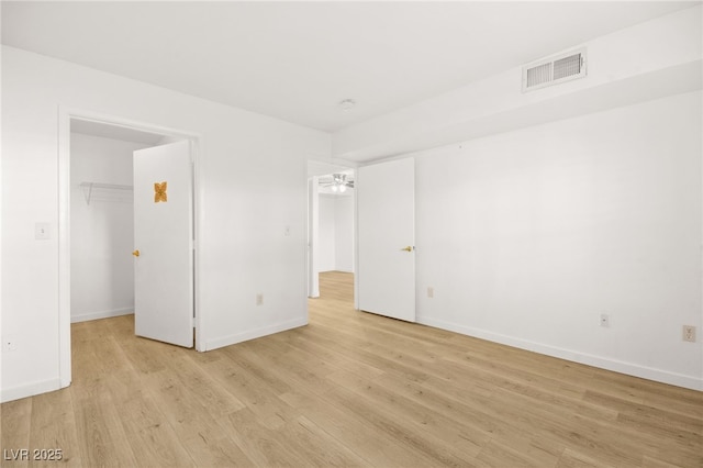 unfurnished bedroom with light wood-style floors, a walk in closet, visible vents, and baseboards