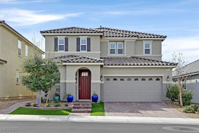 view of front facade with decorative driveway, an attached garage, a tile roof, and stucco siding