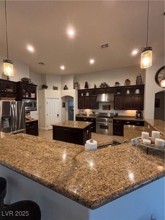 kitchen featuring arched walkways, stainless steel appliances, a spacious island, glass insert cabinets, and under cabinet range hood