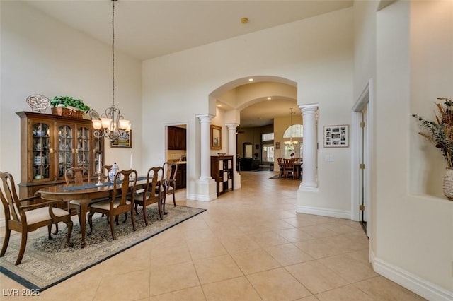 dining space with arched walkways, a high ceiling, light tile patterned flooring, decorative columns, and a chandelier