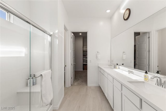 bathroom featuring a spacious closet, a sink, a shower stall, and double vanity