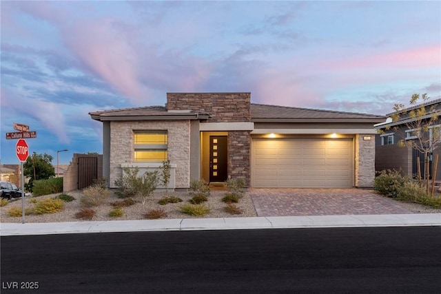 view of front of house featuring decorative driveway, stone siding, and an attached garage