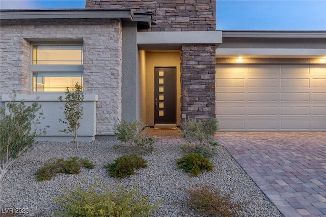 entrance to property with a garage, stone siding, decorative driveway, and stucco siding