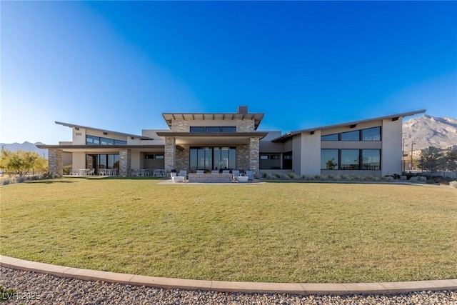 rear view of property featuring stone siding, a lawn, a mountain view, and stucco siding