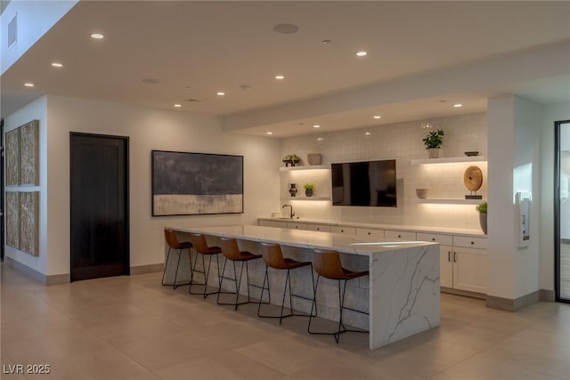 interior space featuring baseboards, a sink, backsplash, and recessed lighting