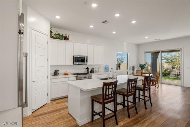 kitchen with visible vents, an island with sink, stainless steel microwave, stove, and light wood-style floors