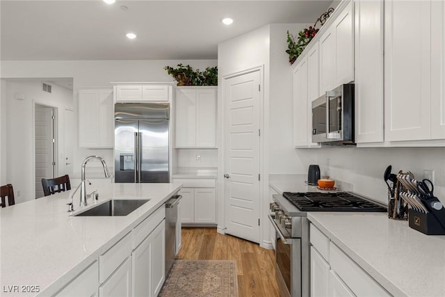 kitchen with a sink, white cabinets, light wood-style floors, light countertops, and high end appliances